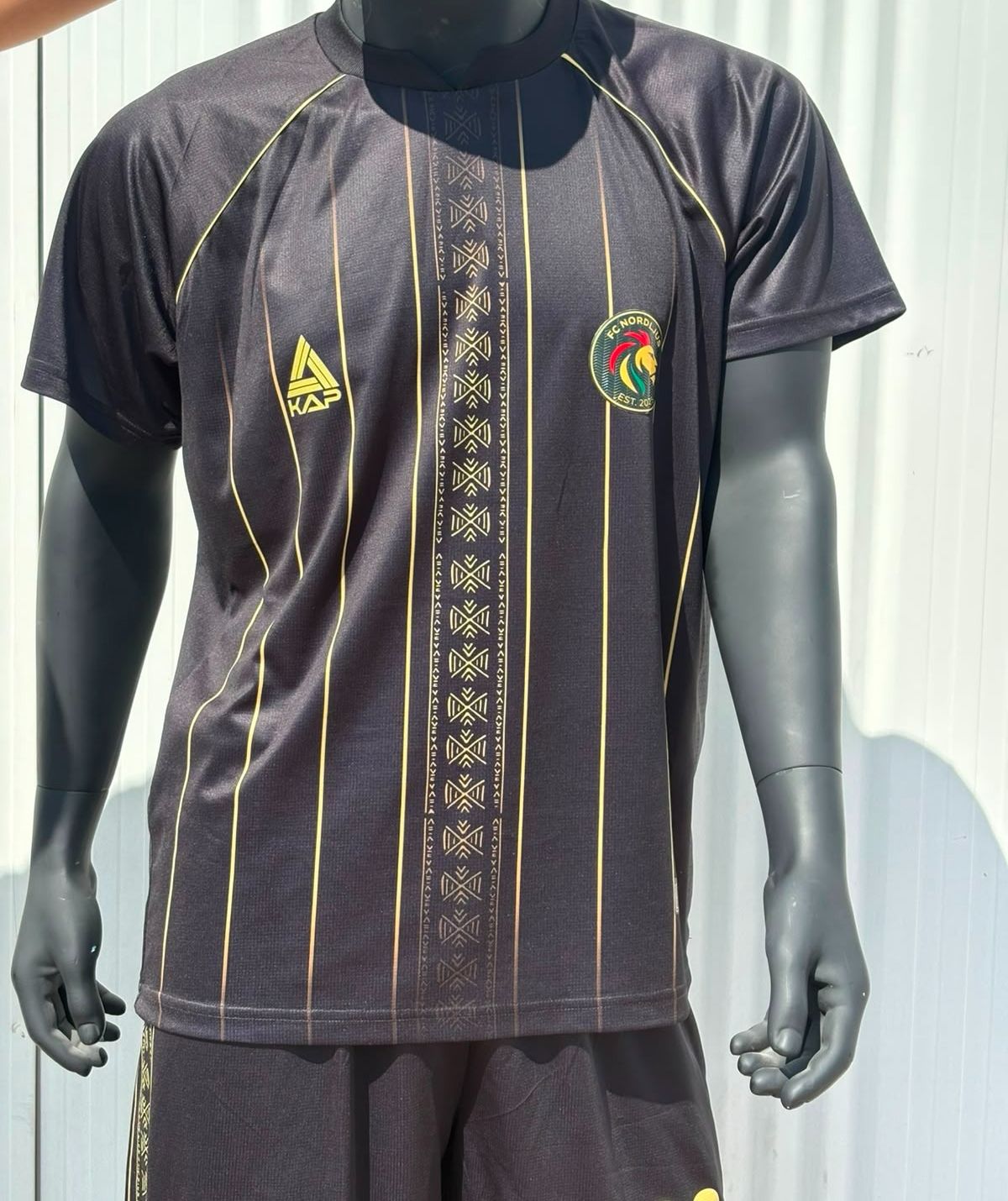 FC Nordljus home shirt: black with gold pinstripes and a patterned centre band