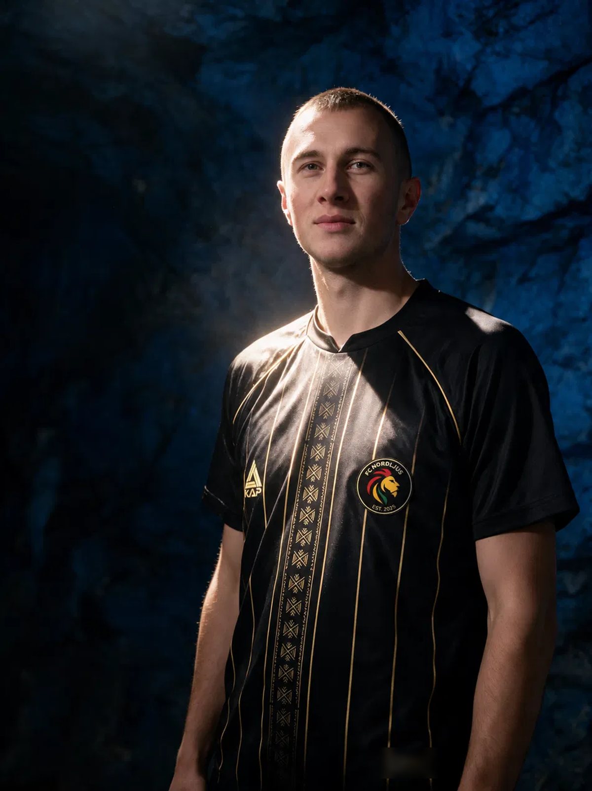 FC Nordljus player in the black and gold 2027 shirt against the blue rock of a Stockholm metro station